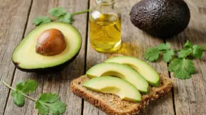 Avocado tagliato e fette su pane ai cereali con una bottiglietta di olio su tavolo di legno