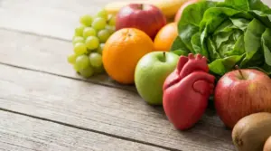 Frutta e verdure fresche con modello anatomico del cuore su tavolo in legno, simbolo di salute cardiovascolare