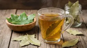 Tazza di tisana all’alloro fumante su tavolo di legno con foglie di alloro fresche e secche accanto