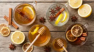 Tazze di bevande calde con cannella e limone su tavolo in legno, con fette di agrumi e spezie