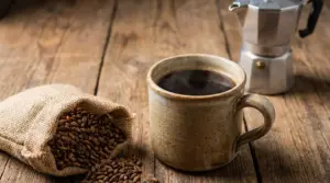 Tazza di caffè d'orzo fumante con chicchi d'orzo e moka su tavolo di legno