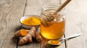 Barattolo di miele con curcuma in polvere e radice fresca su tavolo di legno