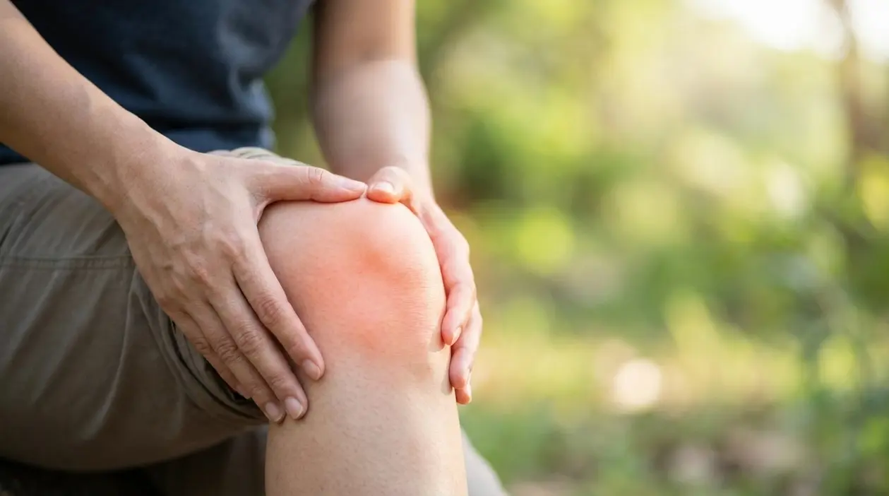 Persona che tiene il ginocchio dolorante con le mani, evidenziando un fastidio articolare.