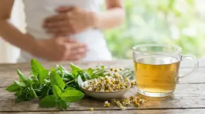 Tisana alle erbe con menta e camomilla su un tavolo, con persona che si tiene l’addome sullo sfondo