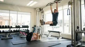 Persone in palestra: un uomo esegue sollevamenti delle gambe alla sbarra e una donna fa crunch su tappetino
