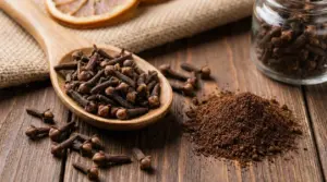 Chiodi di garofano interi in un cucchiaio di legno e polvere di chiodi su un tavolo rustico